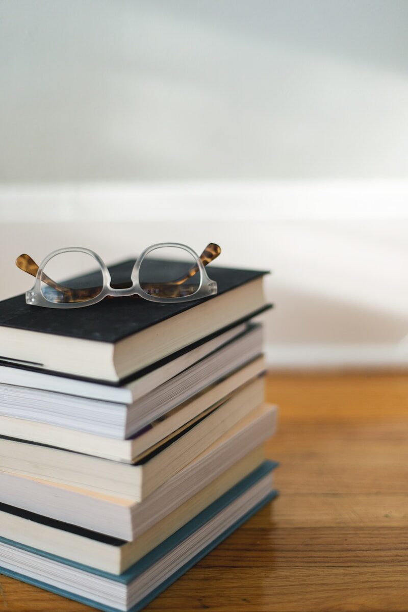 Clear reading glasses rest on a stack of books, emphasizing a cozy reading environment. The image highlights a love for books and knowledge.